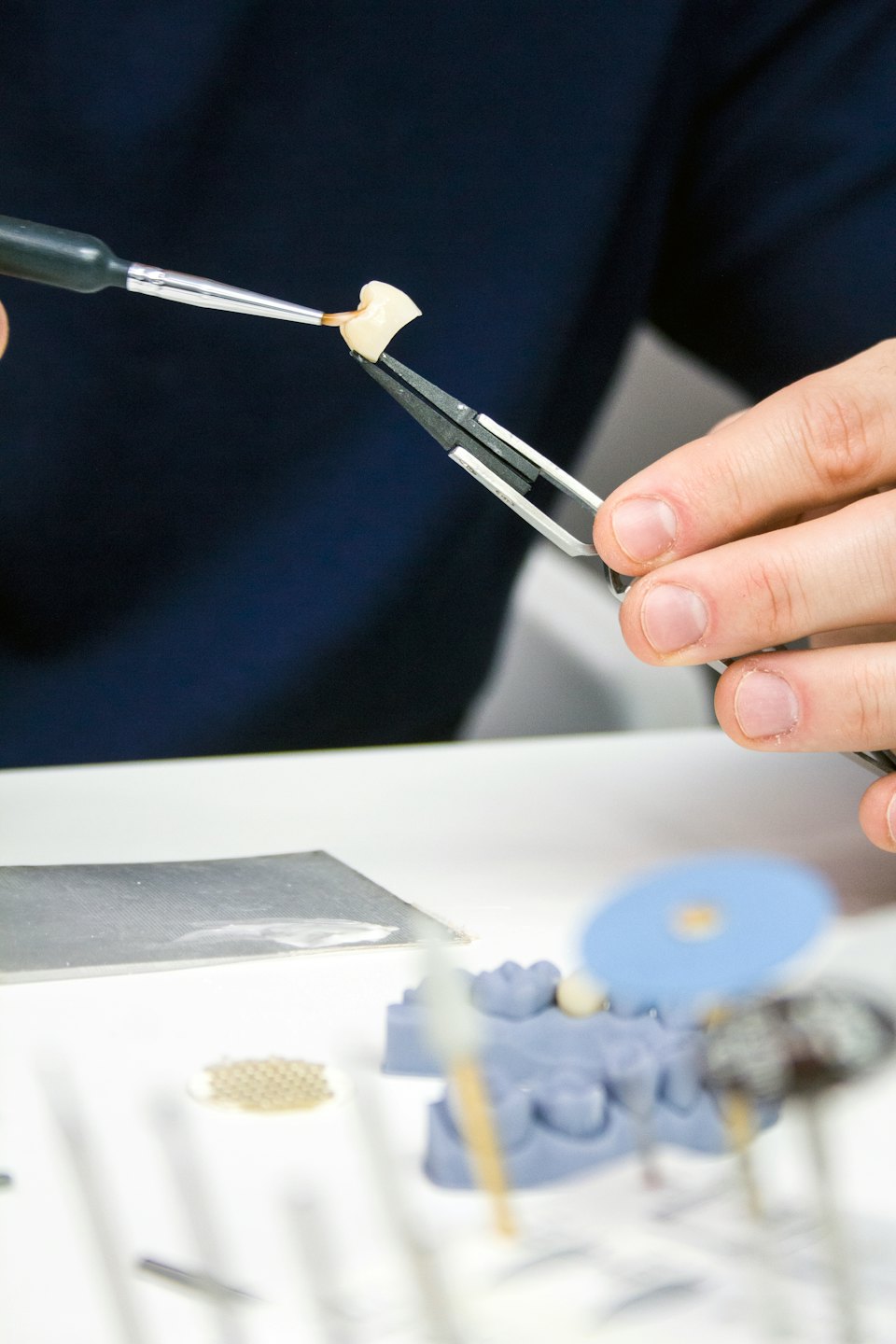 Mani che applicano una sostanza a una corona dentale con un pennello fine.